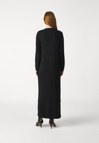 Melna adīta maksi kleita ar garām piedurknēm, apaļu kakla izgriezumu un sānu šķēlumiem apakšmalā. Valkāta ar melnām augstpapēžu kurpēm. Gluda tekstūra.