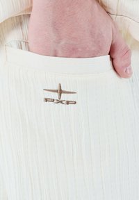 Tejido blanco acanalado con un bolsillo; presenta un logo bordado "PXP" en color marrón claro. La textura parece suave y ligera.