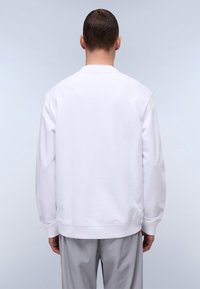 Hvid sweatshirt med lange ærmer, ribbede manchetter og kant, glat stofoverflade. Set fra ryggen, præsenteret mod en lys baggrund.