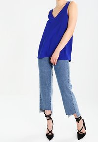 Kungsblå ärmlös topp med V-ringning, parat med ljusblå korta jeans. Utseendet fulländas med svarta snörningsklackar.