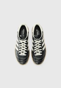 Black leather sneakers with white accents and three stripes, featuring a rounded toe, white laces, textured surface, and rubber sole.