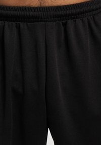 Sorte atletiske shorts med elastisk talje og struktureret stof, der har folder og en glat overflade. Ingen yderligere detaljer synlige.