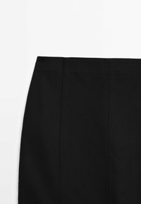 Jupe noire avec des détails de coutures verticales sur un fond blanc uni, montrant la partie supérieure et la ceinture.