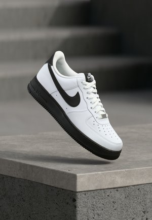 Baskets en cuir blanc avec accents noirs, bout arrondi et détails perforés. Semelle en caoutchouc noire avec motif texturé et fermeture à lacets.