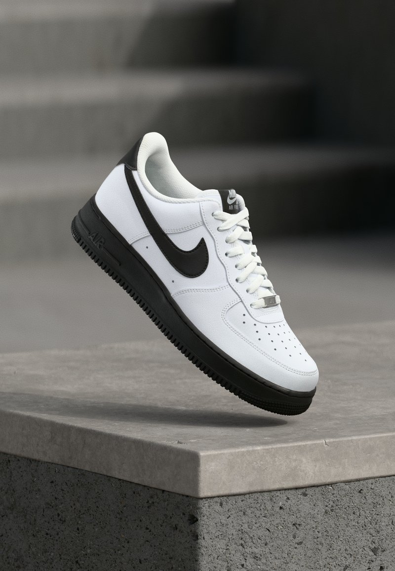 Baskets en cuir blanc avec accents noirs, bout arrondi et détails perforés. Semelle en caoutchouc noire avec motif texturé et fermeture à lacets.