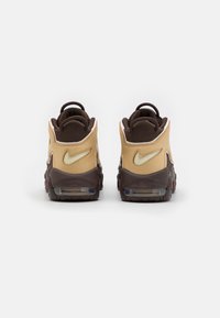 Nike-sneakers med brunt och beige läder, hög design, vadderad krage, synlig luftdämpning och subtil branding på hälen.