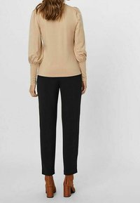 Beige Langarmoberteil mit gerafften Puffärmel, kombiniert mit schwarzen Hosen und braunen Blockabsatz-Stiefeletten. Insgesamt minimalistisches Design.