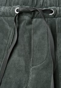 Nära vy av mörkgrå kordbyxor med svart dragsnöre som är trätt genom metallöglor på den elastiska midjan.