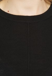 Maglione nero lavorato a maglia con scollatura rotonda, tessuto testurizzato e un sottile dettaglio di cucitura che corre verticalmente al centro.