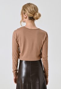 Maglione marrone a maniche lunghe con design aderente, colletto a giro, e lieve rigatura sulle spalle, abbinato a una gonna in pelle nera lucida.
