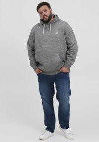 Grauer Hoodie mit Kordelzügen, Fronttasche, gerippten Bündchen und Saum; getragen mit blauen Jeans und weißen Sneakers. Subtile Textur und Logodetail.