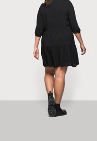 Vestido negro midi con dobladillo en capas y mangas abullonadas de 3/4. Combinado con botas negras hasta el tobillo con suela de goma texturizada.