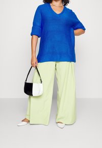 Blå stickad V-ringad tröja med uppvridna ärmar, matchad med ljusgröna vida byxor. Accessoar: liten svart- och vitrandig axelremsväska, vita skor.