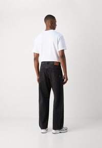 Sorte denim jeans med en løs pasform, høj talje og bagside patch-detajle. Kombineret med en ensfarvet hvid t-shirt med korte ærmer og grå sneakers.