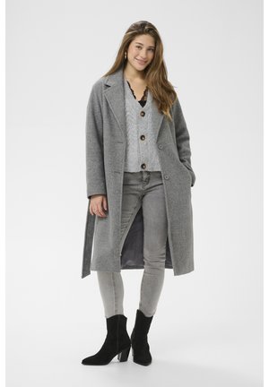 Hosszú szürke gyapjú kabát kihajtott gallérral egy világosszürke kötött pulóver fölött, világosszürke farmerral és fekete sarkú bokacsizmával párosítva.