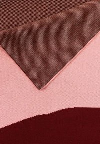 Tkanina z geometrycznym wzorem, na którym strukturalny ciemnoczerwony materiał nakłada się na gładkie różowe i bordowe sekcje.