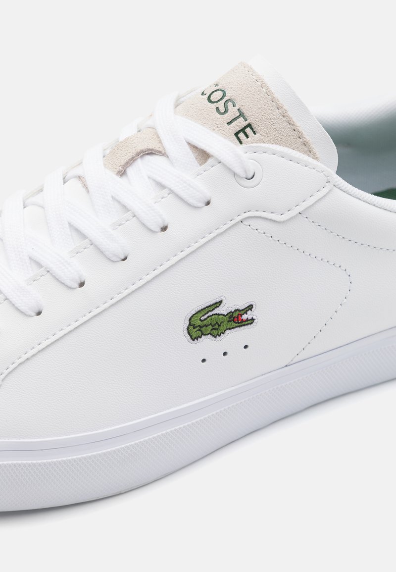 Witte leren sneaker met een gestructureerd oppervlak, groen geborduurd logo, ronde neus en platte witte veters. Lichtgekleurde suède hieltab.