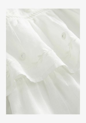 White fabric dress featuring floral embroidery, ruffled hem, and button detailing. Soft texture with a lightweight, flowing design.