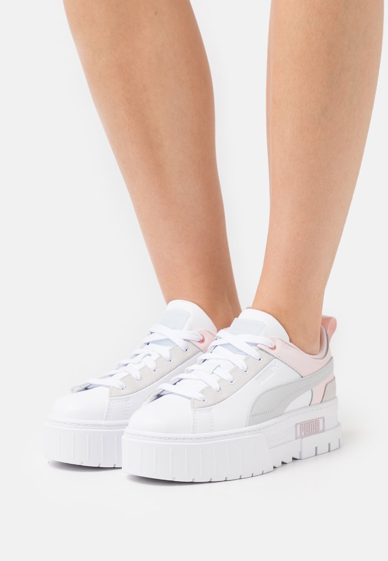 Vita plattformssneakers med rosa och grå accenter, slätt läder, rund tå och vadderad krage. Har en robust gummisula och snörning.