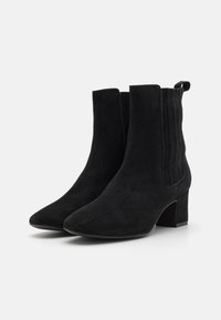 Botas de tobillo de ante negro con punta afilada, paneles laterales elásticos y tacón ancho. Presenta una pestaña en forma de bucle en la parte trasera para facilitar el uso.