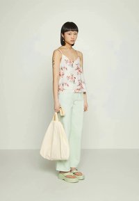 Top de alças leve e floral, com corte solto; calças largas em verde claro. Bolsa de lona creme com alças curtas, sandálias de plataforma verdes.