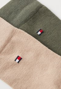 Calcetines de mezcla de algodón en verde oliva y beige claro. Presentan un pequeño logotipo bordado con acentos en rojo, blanco y azul marino. Textura suave, diseño acanalado.