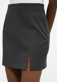 Jupe noire en tissu lisse, avec un design ajusté, dotée d'une fermeture éclair sur le côté et d'une petite fente à l'ourlet pour plus de détails.