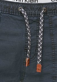 Shorts bleu marine avec une finition texturée, dotés d'une ceinture grise, d'un cordon tressé avec des accents blancs et de bouts en cuir.
