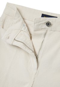 Pantaloni in corduroy crema con zip e chiusura a bottone. Presentano un tessuto testurizzato con righe verticali e cuciture resistenti.