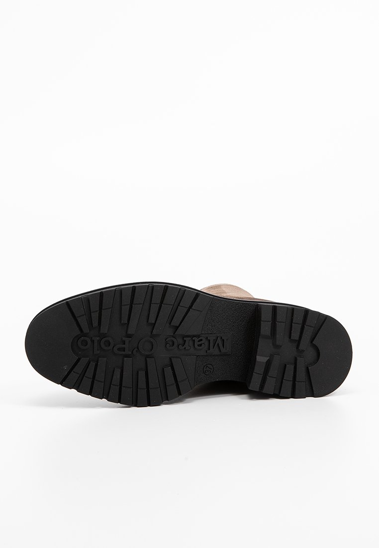 Schwarze Gummisohle mit tiefem Profil, mit eingeprägtem Logo. Oberteil aus hellbraunem Wildleder, das für Haltbarkeit und Griffigkeit ausgelegt ist.