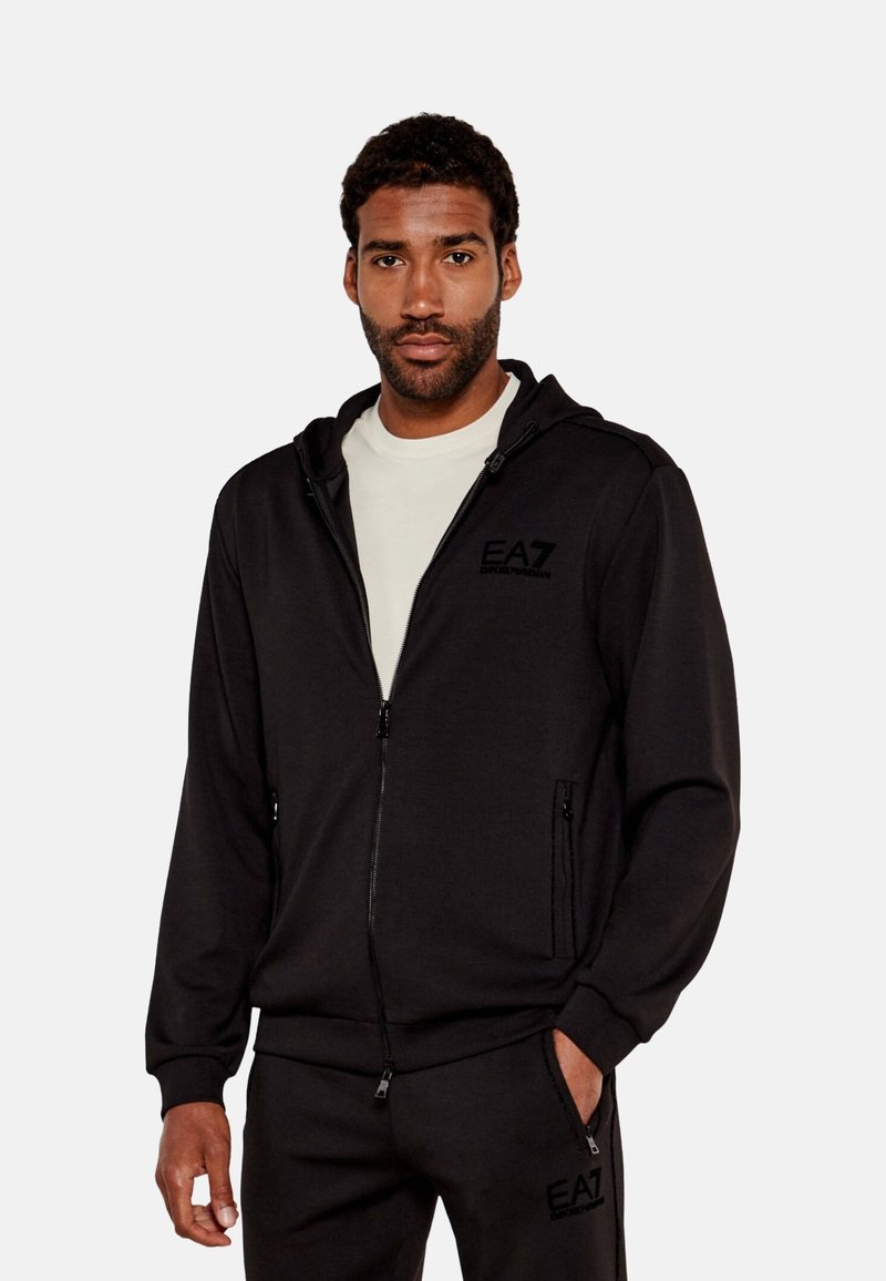 Sudadera con cremallera de color negro, hecha de una tela suave, cuenta con capucha ajustable, bolsillos laterales y un logotipo bordado de EA7 en el pecho.