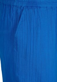 Tessuto blu con trama e righe verticali, dotato di una cintura elastica e di una tasca laterale. Il materiale sembra leggero e traspirante.
