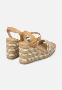 Tan lederen wedge sandalen met gevlochten jute zolen, voorzien van witte kraalaccenten en een verstelbare enkelband. Hoge, gestructureerde hielen.