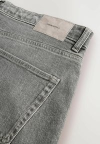 Pilki džinsai su lygiu paviršiumi, turintys išsiskiriančią odinę etikę su užrašu "DENIM SUPPLY" ir kontrastingomis siūlėmis.