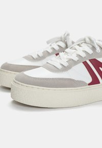 Weiße und graue Sneakers mit einer strukturierten Gummisohle, Wildlederakzenten und roten Designelementen. Ausgestattet mit weißen Schnürsenkeln und einer abgerundeten Zehenform.