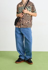 Chemise à manches courtes avec motif abstrait marron, noir et vert ; jean bleu ample ; baskets noires ; petit sac bandoulière.