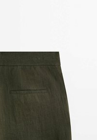 Pantalon en lin vert olive avec une taille élégante et une poche arrière unique dotée d'une fermeture à rabat discrète. Surface texturée visible.