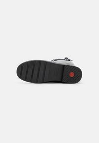 Suola nera di una sneaker con gomma texturizzata per una buona aderenza. Presenta un accento circolare rosso e audaci strisce orizzontali per migliorare la trazione.