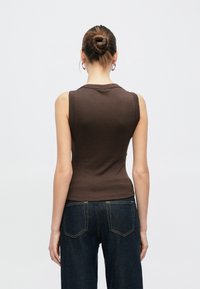 Rjav brezrokavnik iz gladkega blaga s prilegajočim se krojem. Nošen z temno modrimi visokim pasom kavbojkami, ki poudarjajo čisto silhueto.