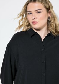 Camisa negra de botones con una textura suave y cuello, que presenta un corte relajado y un brillo sutil.