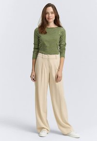 Grün-weiß gestreiftes Hemd kombiniert mit hoch taillierter, beige weiter Hose und weißen Turnschuhen, die eine lockere und moderne Silhouette bieten.