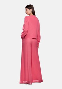 Rosa Strickpullover und weit geschnittene Hose, beide aus einem weichen, fließenden Stoff. Der Pullover hat einen gerippten Saum, und die Hose hat ein leicht durchscheinendes Aussehen.