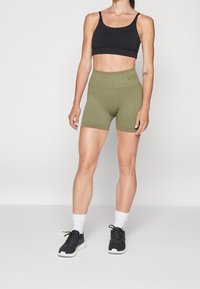 Schwarzer, gerippter Sport-BH und olivgrüne, gerippte High-Waist-Shorts, kombiniert mit weißen Socken und schwarzen Sportschuhen. Glatte Textur, enganliegende Passform.