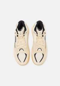 Beige high-top sneakers med sorte accenter, teksturerede paneler, snørebånd og en gummisål. Funktionen inkluderer ovale udskæringer og polstring rundt om kraven.