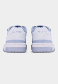 Ζευγάρι λευκών και ανοιχτό μπλε παπουτσιών Lacoste, που φαίνεται από πίσω με εμφανές το όνομα της μάρκας στην ταμπέλα της φτέρνας και στη σόλα.