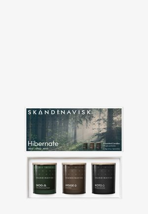 Zestaw świec zapachowych w białym pudełku zawiera trzy szklane słoiki — ciemnozielony, brązowy i czarny — z drewnianymi pokrywkami, oznaczone nazwami Skog, Hygge i Koto.