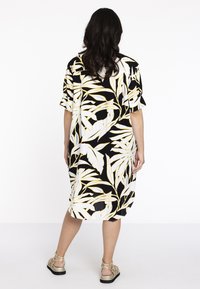 Schwarz-weißes Kleid mit gelben Blättermustern, lockere Passform, kurze Ärmel, knielange Länge, aus leichtem Stoff hergestellt.