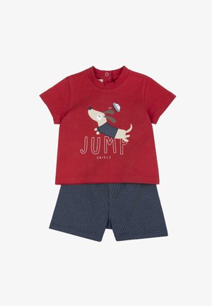 Chemise rouge à manches courtes avec une illustration d'un chien sautant portant un chapeau de marin et un short bleu marine à petits pois blancs.