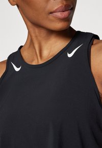 Camiseta sin mangas deportiva negra hecha de una tela suave. Presenta acentos en blanco del logo de Nike en los hombros y un diseño de cuello redondo.