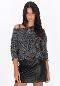 Pulover negru și alb, tricotat, cu umerii lăsați și un model în diamant, având o margine desfăcută, asortat cu o fustă mini din piele neagră, cu o fanta în partea din față.